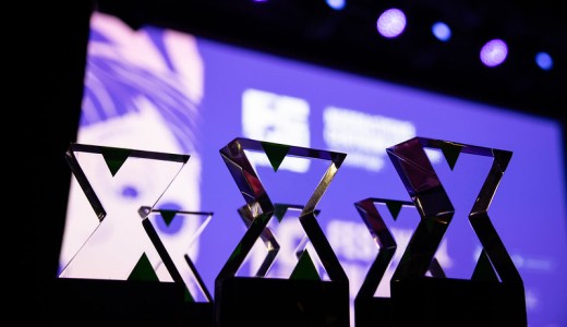 Zbliżenie na kilka statuetek ustawionych na scenie; w tle rozmyte, fioletowo-niebieskie oświetlenie i ekran