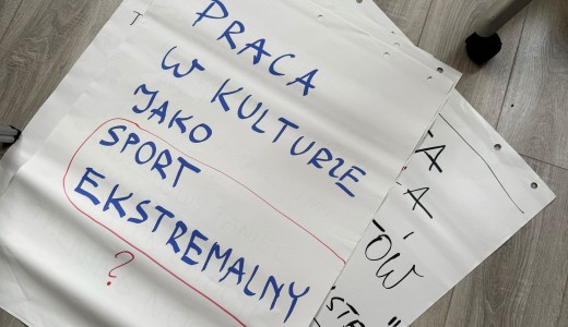 na drewnianej podłodze leży kartka z napisem "praca w kulturze jako sport ekstramalny?"