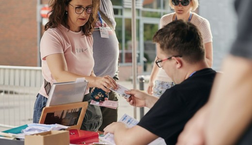 zdjęcie kobiety kupującej bilet. Zdjęcie na zewnątrz, w tle kobieta i mężczyzna, budynki