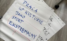 na drewnianej podłodze leży kartka z napisem "praca w kulturze jako sport ekstramalny?"