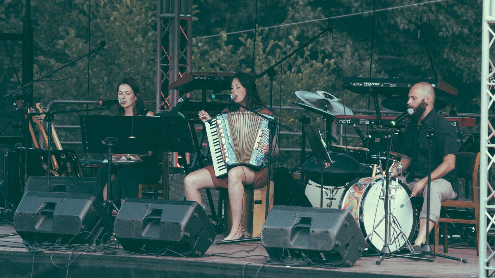 troje muzyków siedzi z instrumentami na scenie