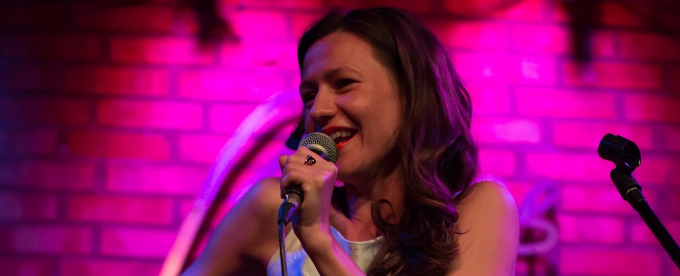 Na zdjęciu widać artysktę Renatę Irsa w czasie śpiewania. Artyka trzyma mikrofon, w tle widać ceglaną ścianę. Koncert odbędzie się 25 kwietnia 2021 na antenie Radia Gdańsk
