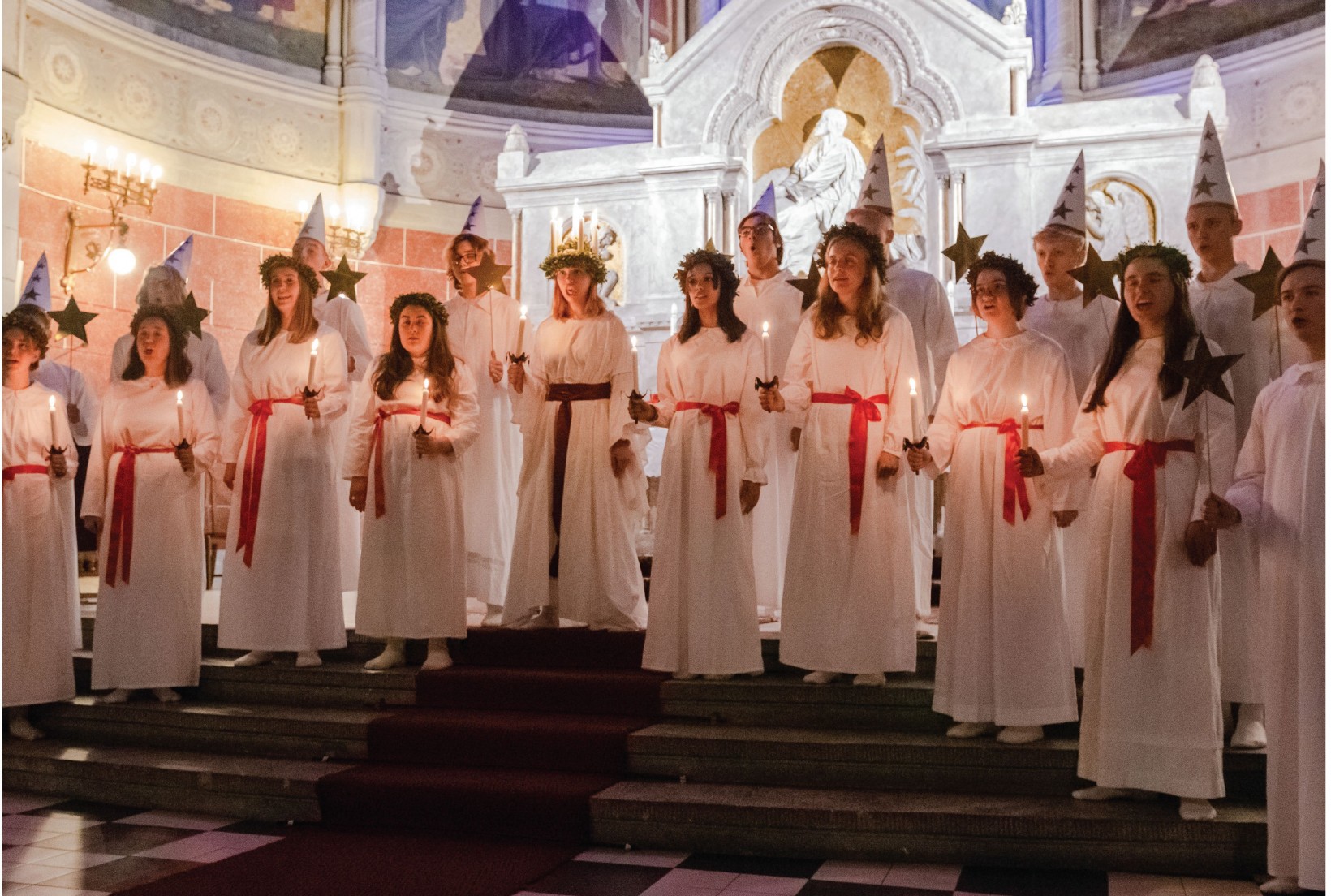 zdjęcie przedstawiające dziewczęta w białych szatach z wiankami ze świec na głowie 