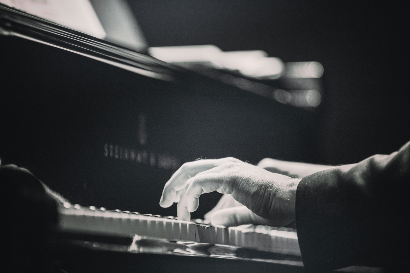 Czarno-biała fotografia dłoni uderzających w kalwiaturę fortepianu