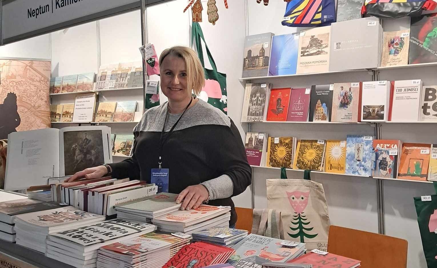 zdjęcie stoiska targowego Nadbałtyckiego Centrum Kultury w Gdańsku, kobieta za ladą, wokół na półkach i ladzie publikacje