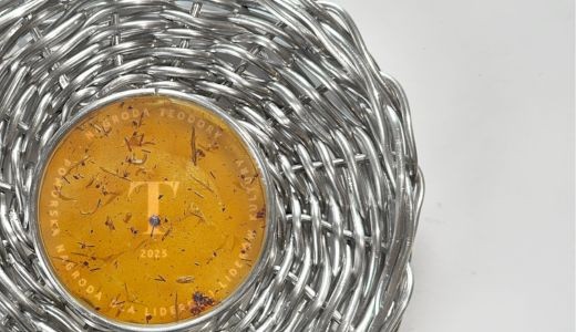 fragment zdjęcia statuetki Nagrody Teodory, pleciony jak kosz wiklinowy kosz wieniec, w środku plakieta bursztynowa z bioplastiku i wygrawerowaną literą "T"