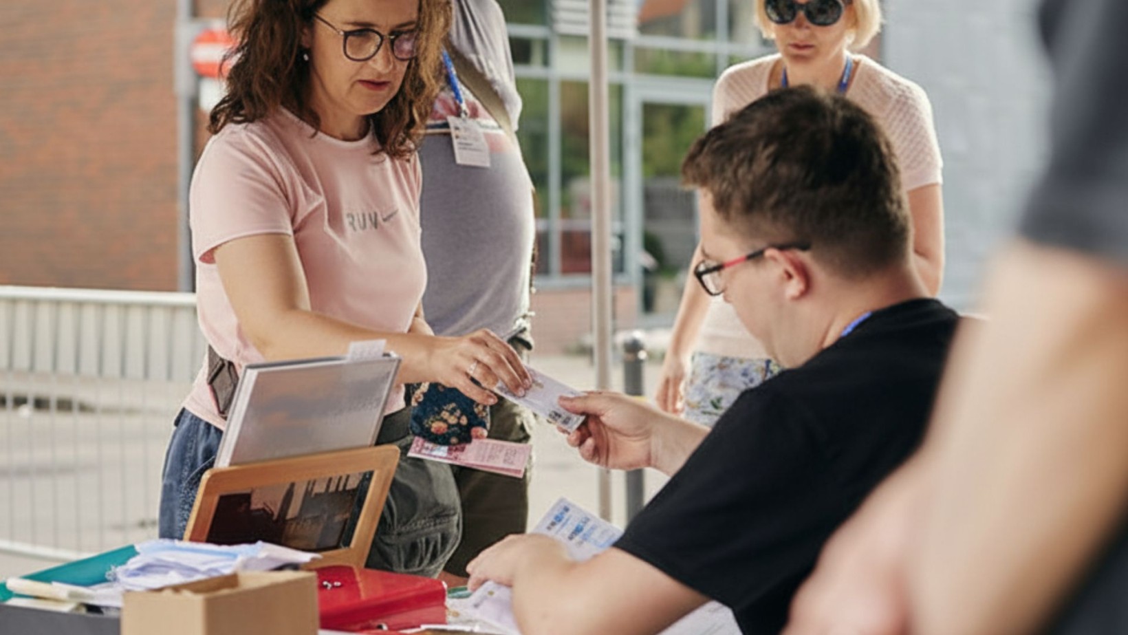 zdjęcie kobiety kupującej bilet. Zdjęcie na zewnątrz, w tle kobieta i mężczyzna, budynki