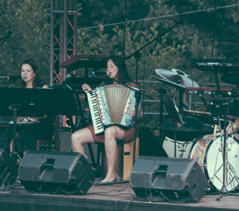troje muzyków siedzi z instrumentami na scenie