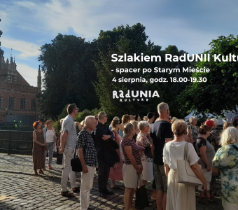 zdjęcie podczas spaceru, na nim ratusz staromiejski, kilkanaścioro ludzi, napisy z nazwą wydarzenia, godziną, dekoracjami w motywie NCK