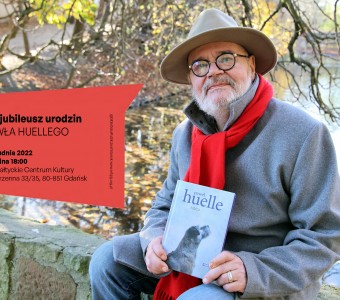 zdjęcie mężczyzny, broda okulary, siedzi na zewnątrz na murku, w tle staw. Prezentuje książkę
