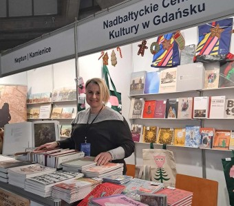 zdjęcie stoiska targowego Nadbałtyckiego Centrum Kultury w Gdańsku, kobieta za ladą, wokół na półkach i ladzie publikacje