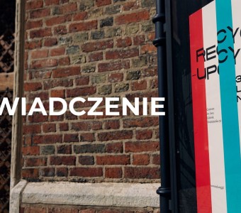 zdjęcie plakatu wystawy Recycle-upcycle w gablocie. W tle ceglana ściana i fragment wrót Centrum św. Jana